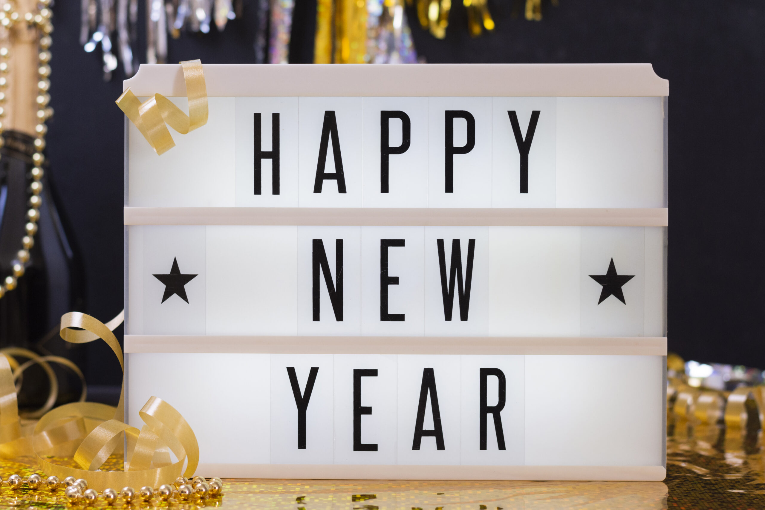 A lightbox sign with the message "HAPPY NEW YEAR" in bold letters, surrounded by festive golden ribbons and decorations