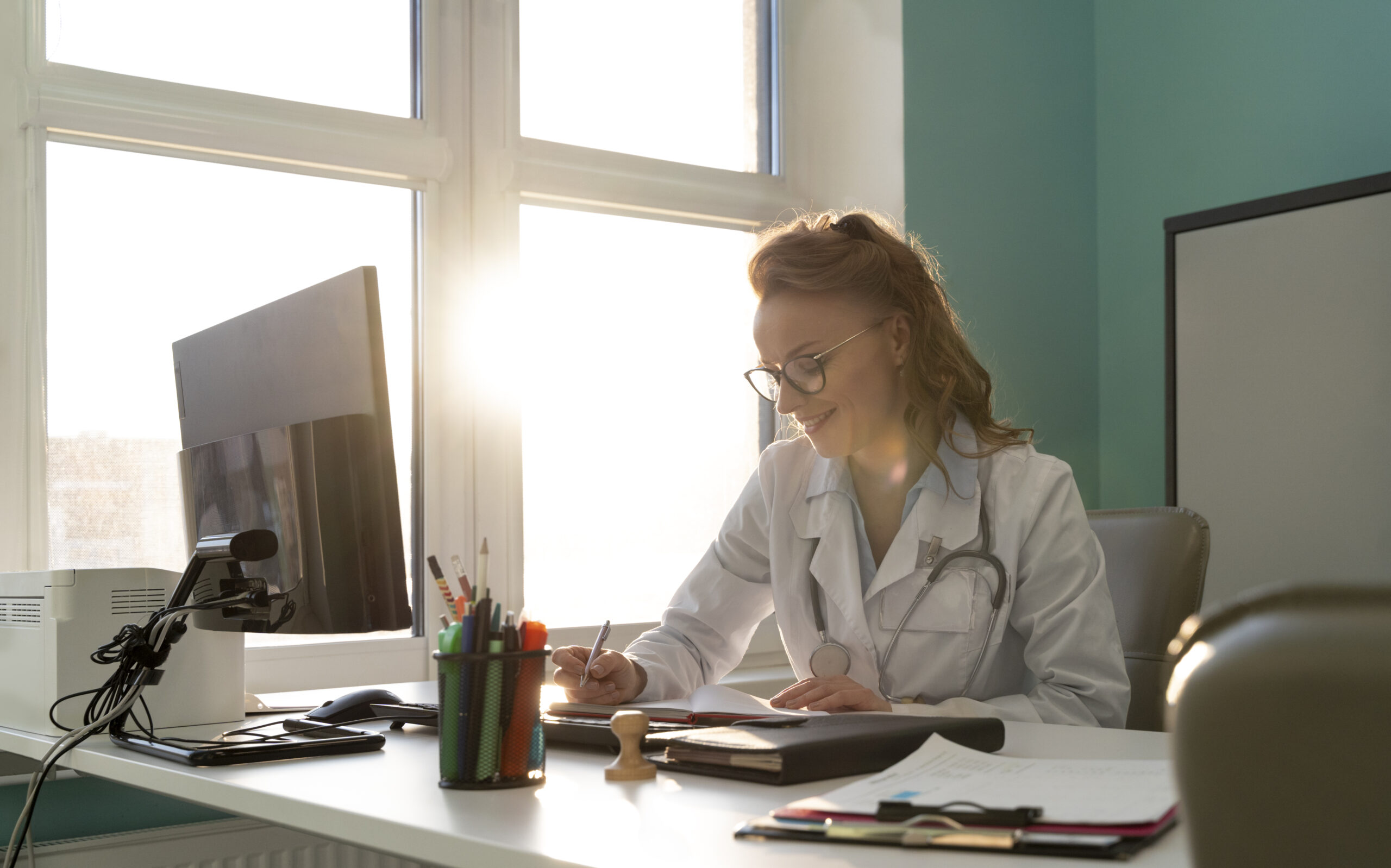 A woman working at a desk with sunlight streaming through a window.