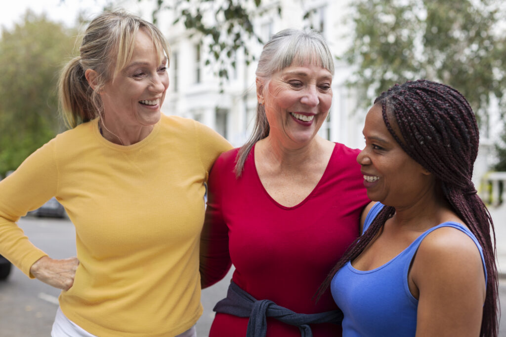 Three women standing outside and smiling while talking and embracing each other.