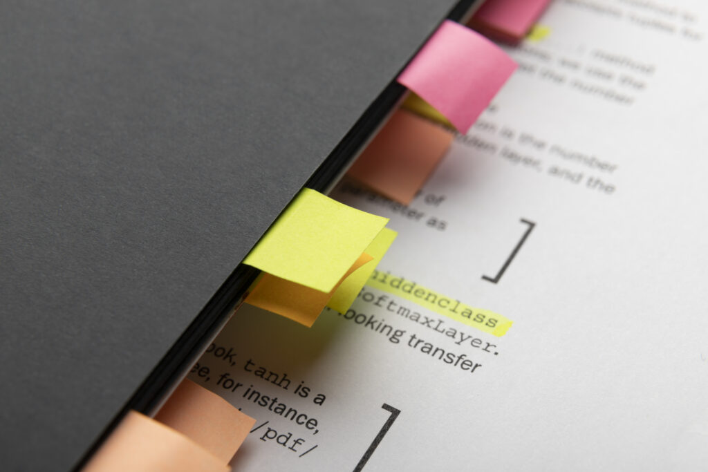 Close-up of a document marked with colourful sticky tabs and highlighted text, partially covered by a black folder.