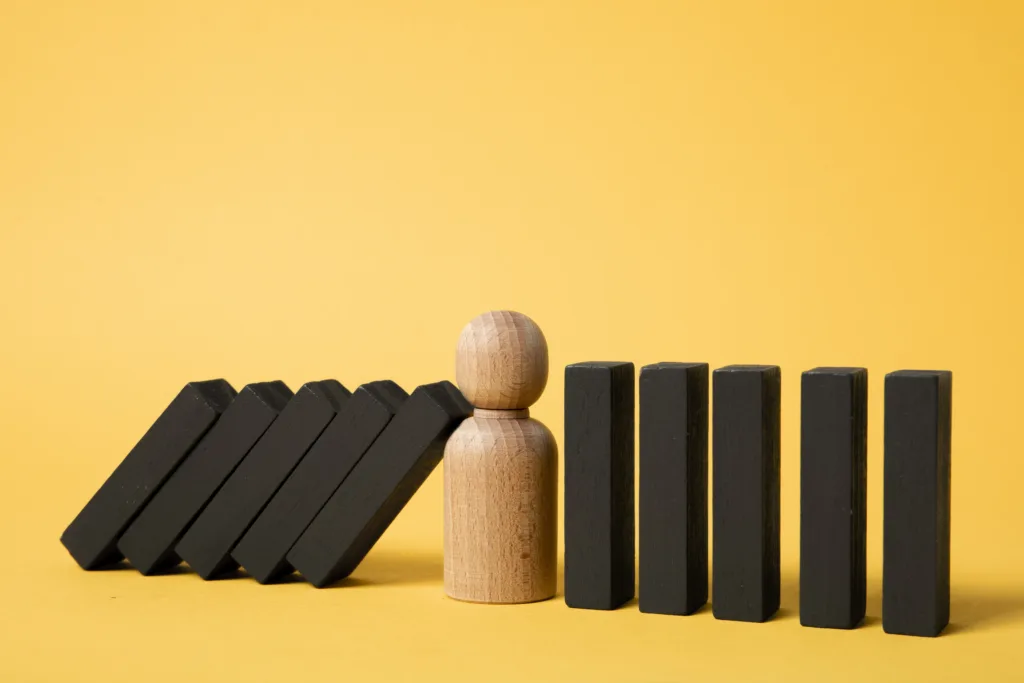 A wooden figure standing upright between falling black domino blocks on a yellow background.