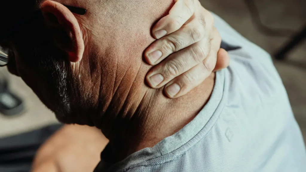 Close-up of a person holding the back of their neck, suggesting neck pain or stiffness.