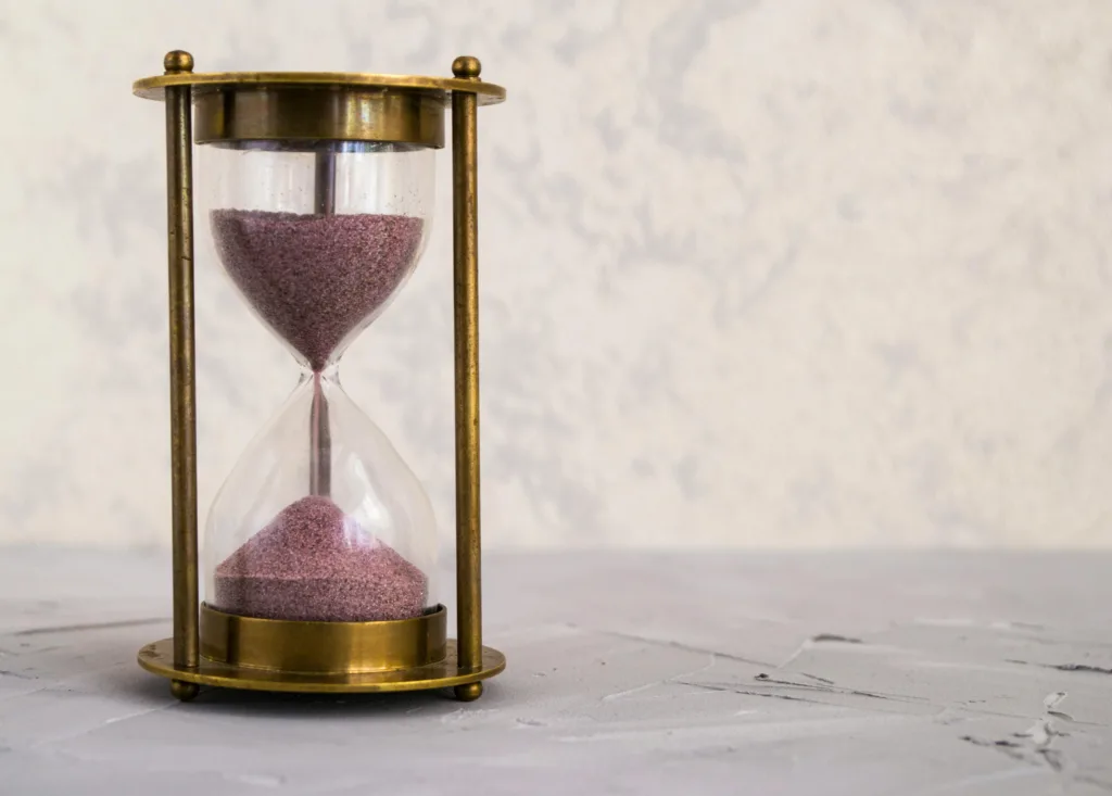 A glass hourglass with pink sand on a light surface.