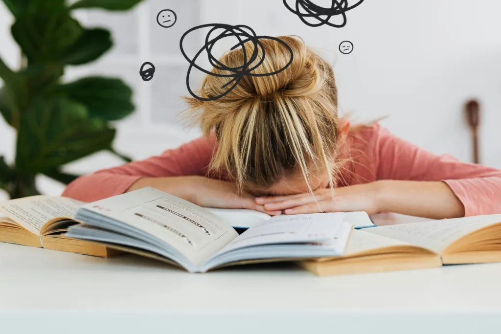 Person resting head on open books with scribble drawings above