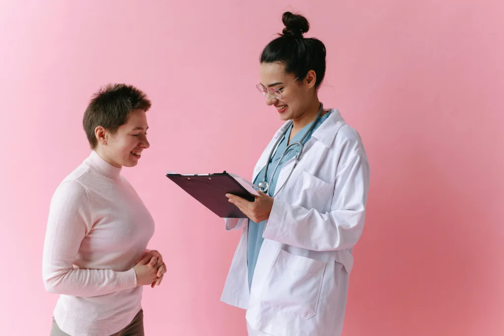 Doctor holding a clipboard and speaking with a patient against a pink background