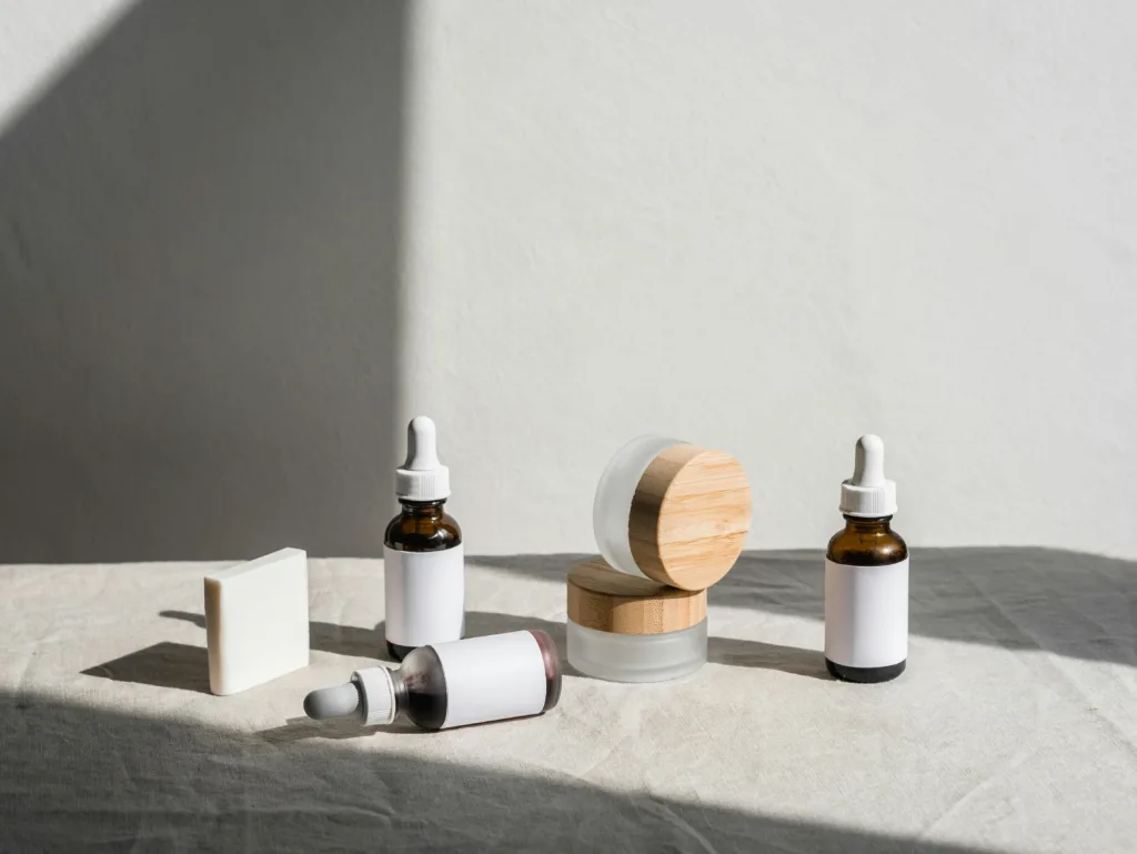 A collection of tubs and small glass bottles with eyedroppers on an off-white background.