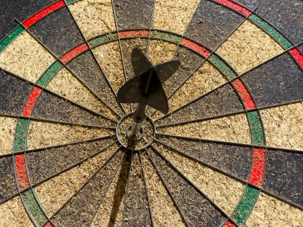 Close up of a dart hitting the bullseye on a rough-textured dartboard.