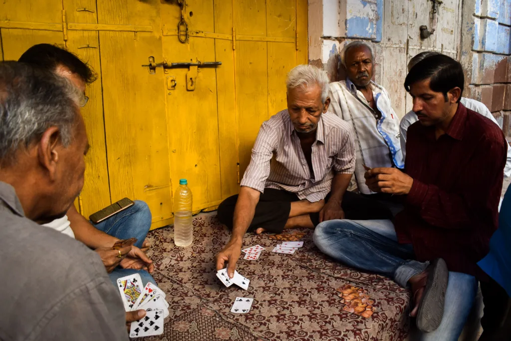 A group of older men in India, seated on the floor playing a card game.