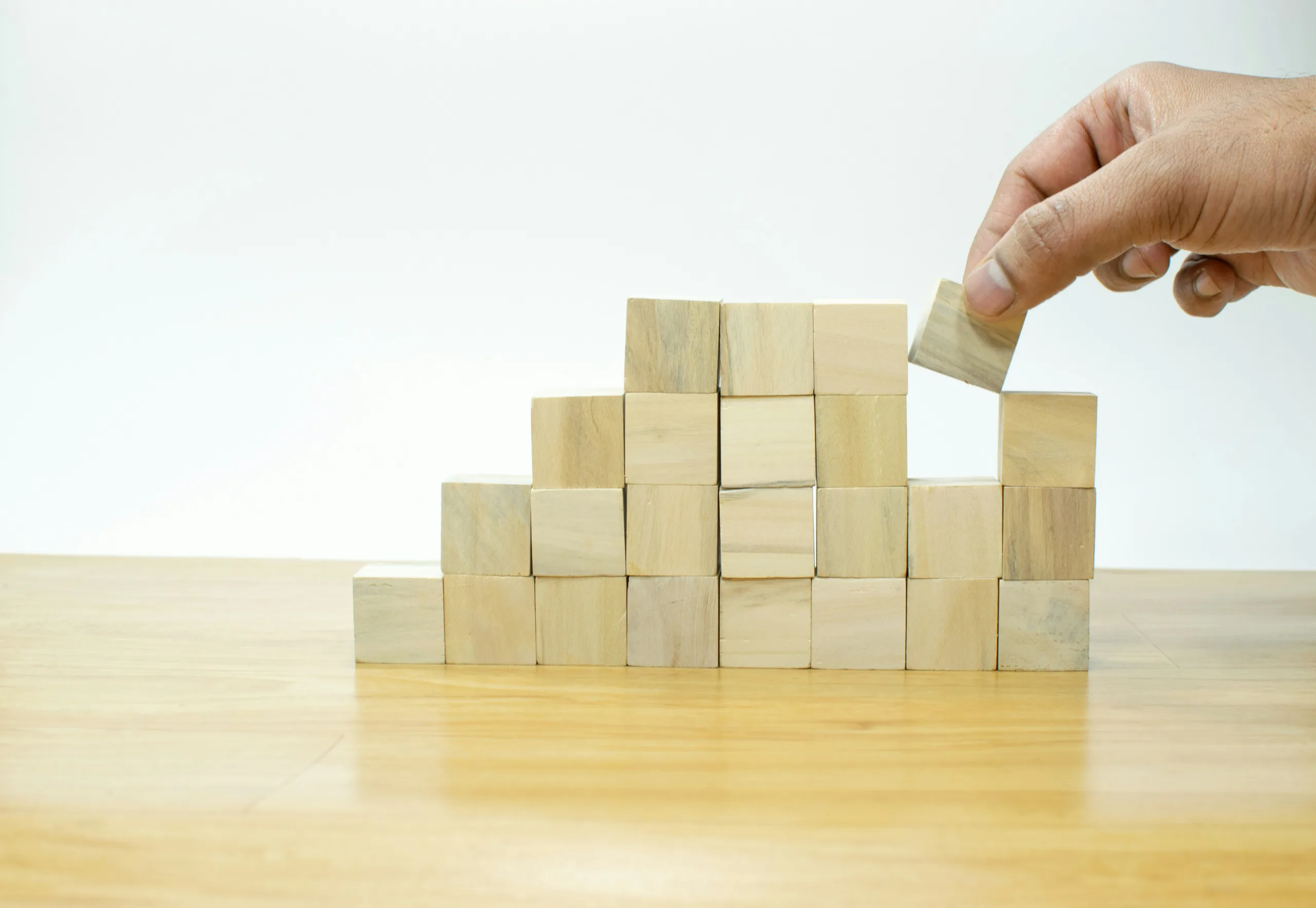 A stack of small wooden blocks on a table, with a hand placing a block in one of the gaps.