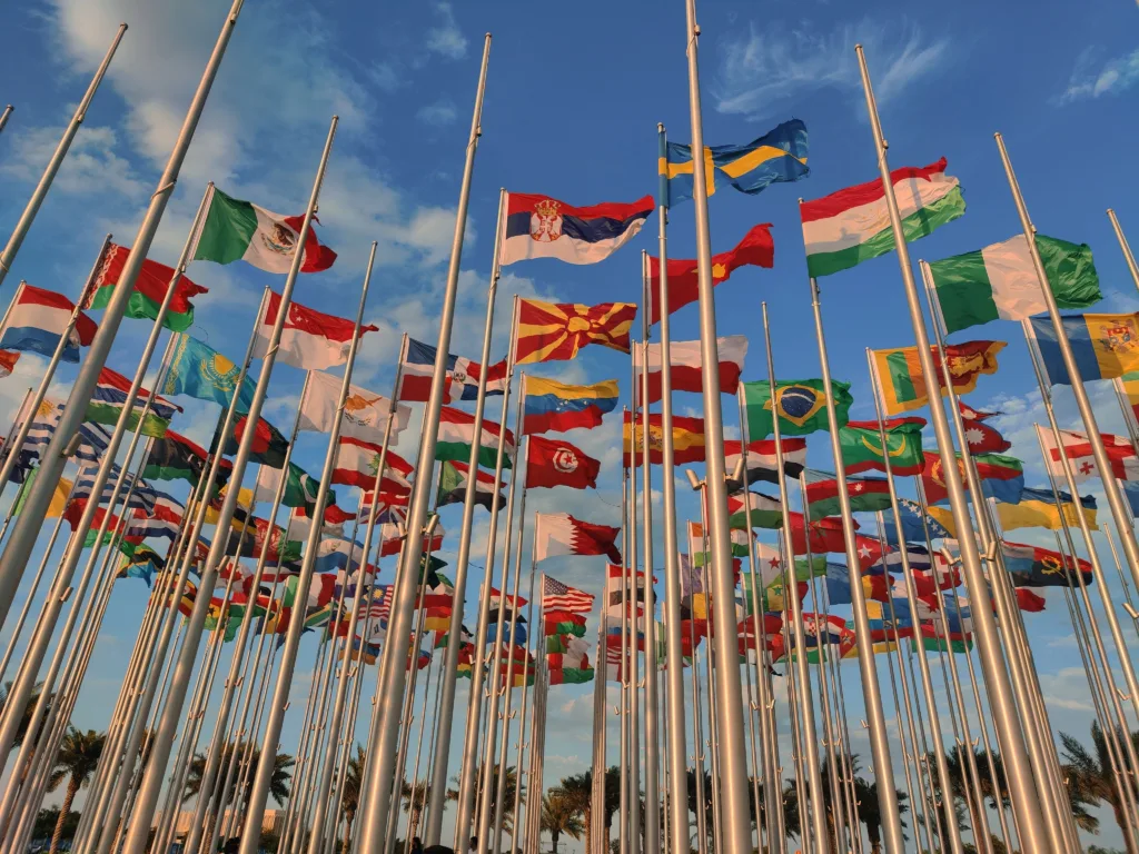 Low-angled shot of many nation’s flags flying against a blue sky.