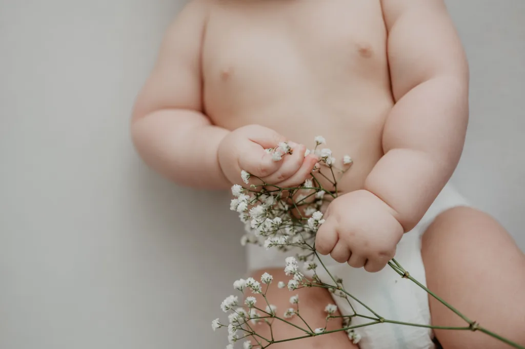 Close-up of a baby’s torso, in the baby’s hand is a sprig of gypsophila ("baby's breath") flowers.