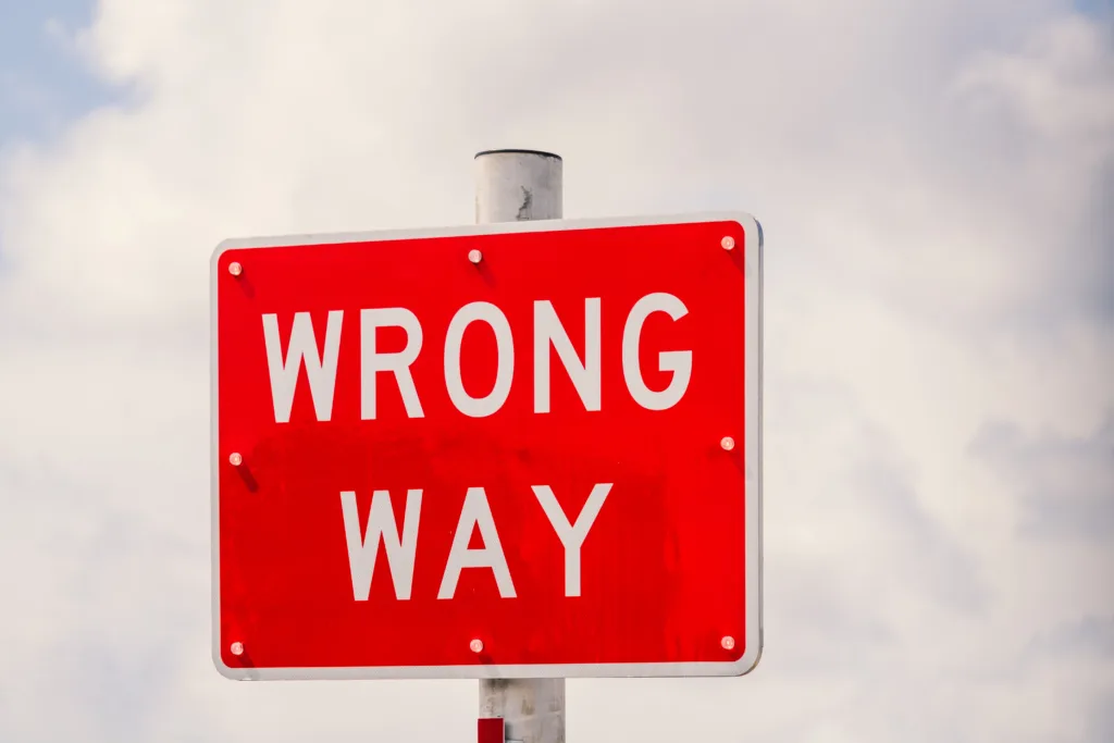 Clear image of a bright red 'Wrong Way' traffic sign against a cloudy sky