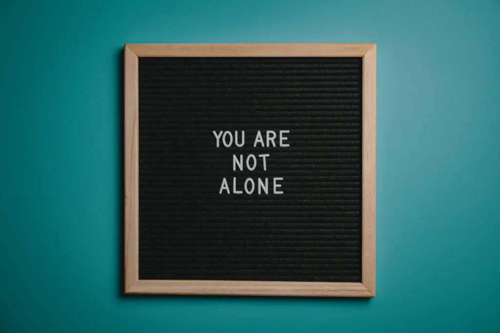 A wooden letter board displays a motivational message 'You are not alone' against a teal background