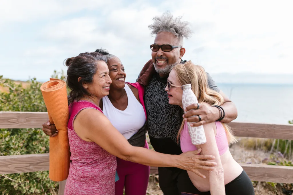 Happy senior friends embracing after a yoga session by the beach, enjoying the outdoors together