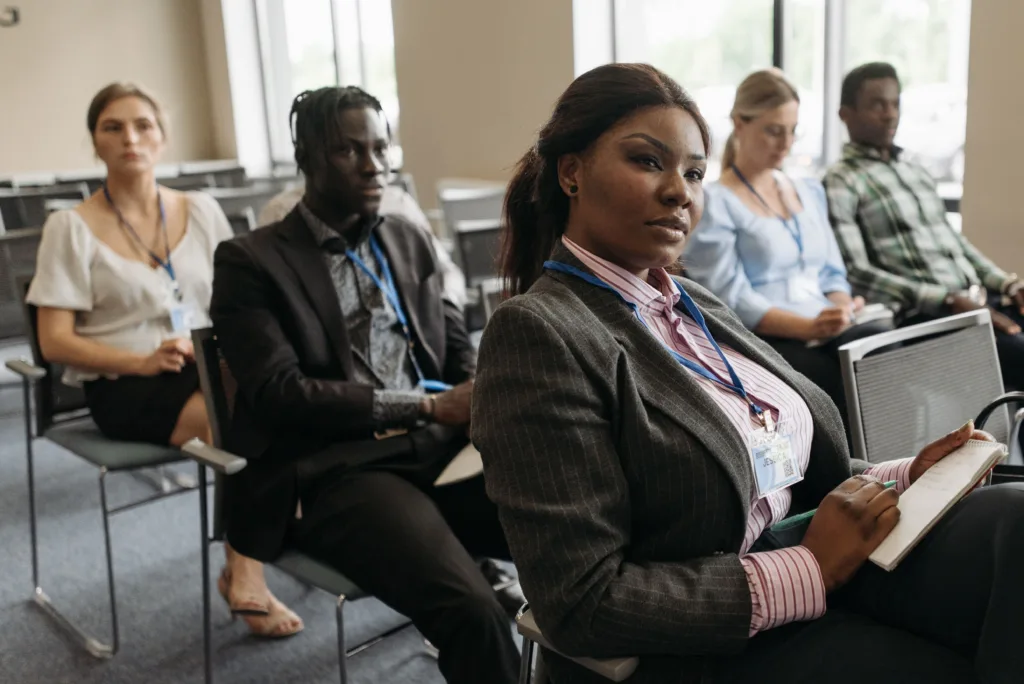 A diverse group attentively listens in a business seminar setting, indoors with notebooks
