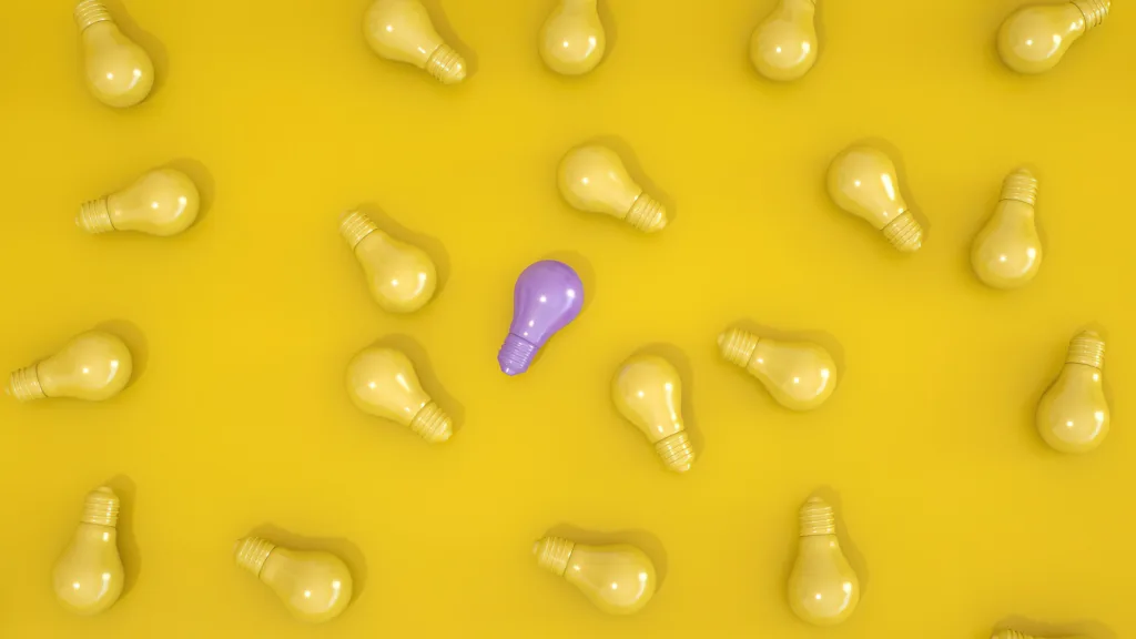 Standout purple light bulb among yellow bulbs on a yellow surface symbolising individuality