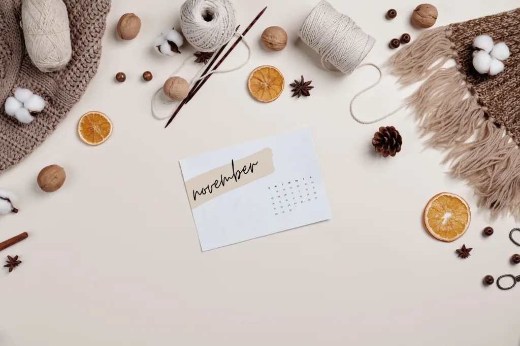 Flat lay of a cosy autumn setup with a November calendar, yarn, and dried oranges