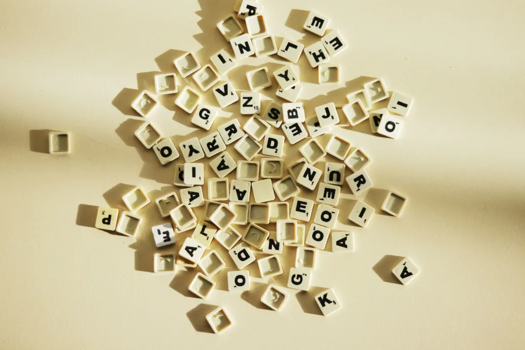 Many Scrabble letter tiles in a messy pile on a beige background.