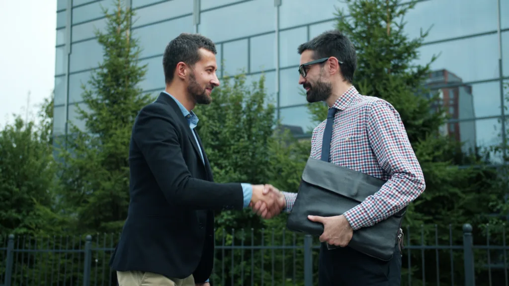 Two businessmen shaking hands outside a modern office building.