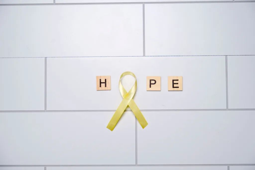 A yellow ribbon forming the letter ‘O’ in the word 'Hope' spelled with letter tiles on a white tiled background.