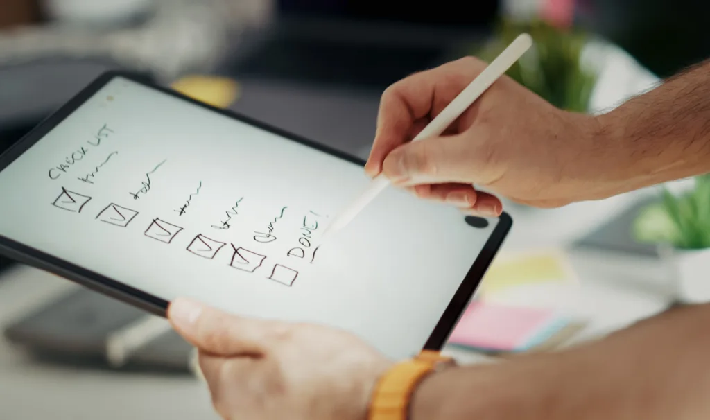 Close-up of a hand writing on a digital checklist using a stylus on a tablet.